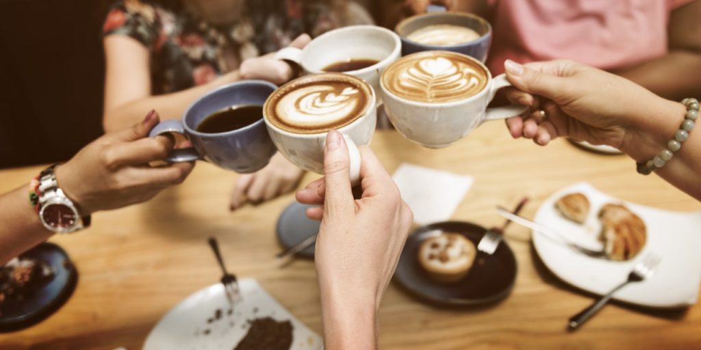 several sets of hands clinking coffee cups together