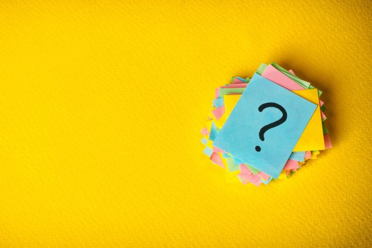 pile of post-it notes with question mark symbol written on top note.